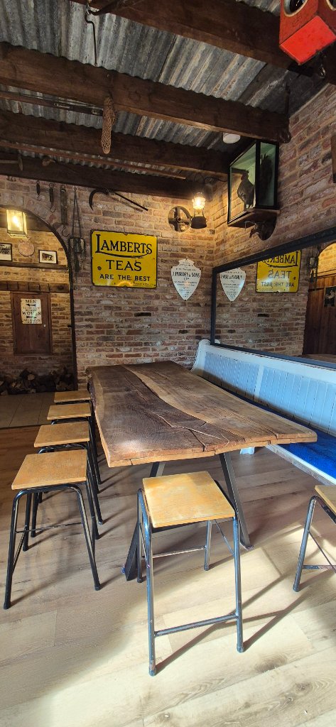 Long live-edge wooden table with stools, exposed brick walls and vintage Lamberts Teas sign — ideal meeting layout