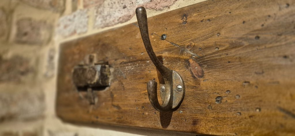 Rustic wooden coat rack with dark metal hook mounted on weathered oak, brick wall beyond